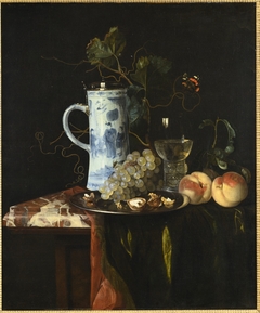 Stilleven met een kan van chinees porselein, druiven, walnoten, roemer, perziken en een kleed op een marmeren tafel by Hendrick Fromantiou